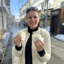 Esbe on a snowy street in Japan, holding two steamed buns